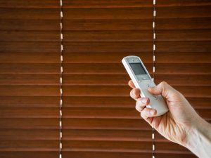 Hand holds a remote control to open the motorised blinds